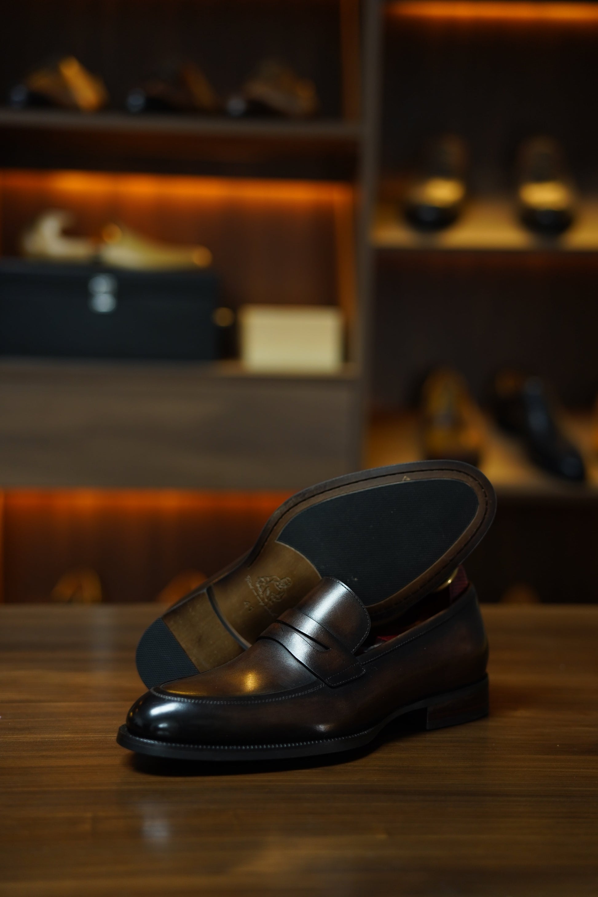 Hand-Burnished Brown Leather Penny Loafers – pair resting on a wooden surface, with one shoe showing the outsole, highlighting the hand-polished finish and comfort.