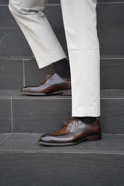 A man wearing Hand-Burnished Chestnut Split-Toe Derby shoes with light trousers, standing on steps outdoors.
