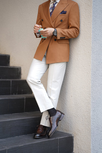 A man wearing HolloShoe Hand-Burnished Chestnut Split-Toe Derby shoes with light trousers and a brown blazer, leaning against a wall outdoors.