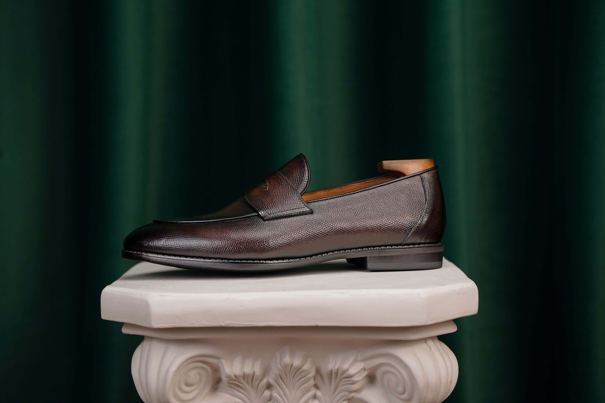 Hand-Finished Espresso Brown Leather Penny Loafers – worn by a man in light trousers, sitting on a classical pedestal, showcasing sophisticated urban look and Blake-stitched construction.
