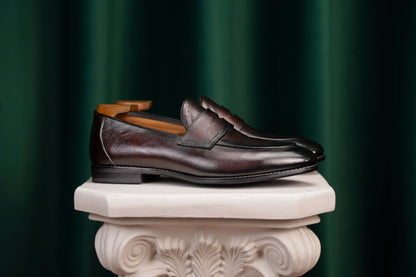 Hand-Finished Espresso Brown Leather Penny Loafers – side view on a white classical pedestal, showcasing rich hand-finished brown leather and subtle heel support.