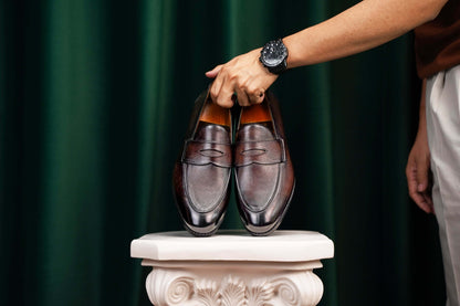 Hand-Finished Espresso Brown Leather Penny Loafers – pair held by a man's hand with a watch, highlighting hand-finished brown leather and classic design.