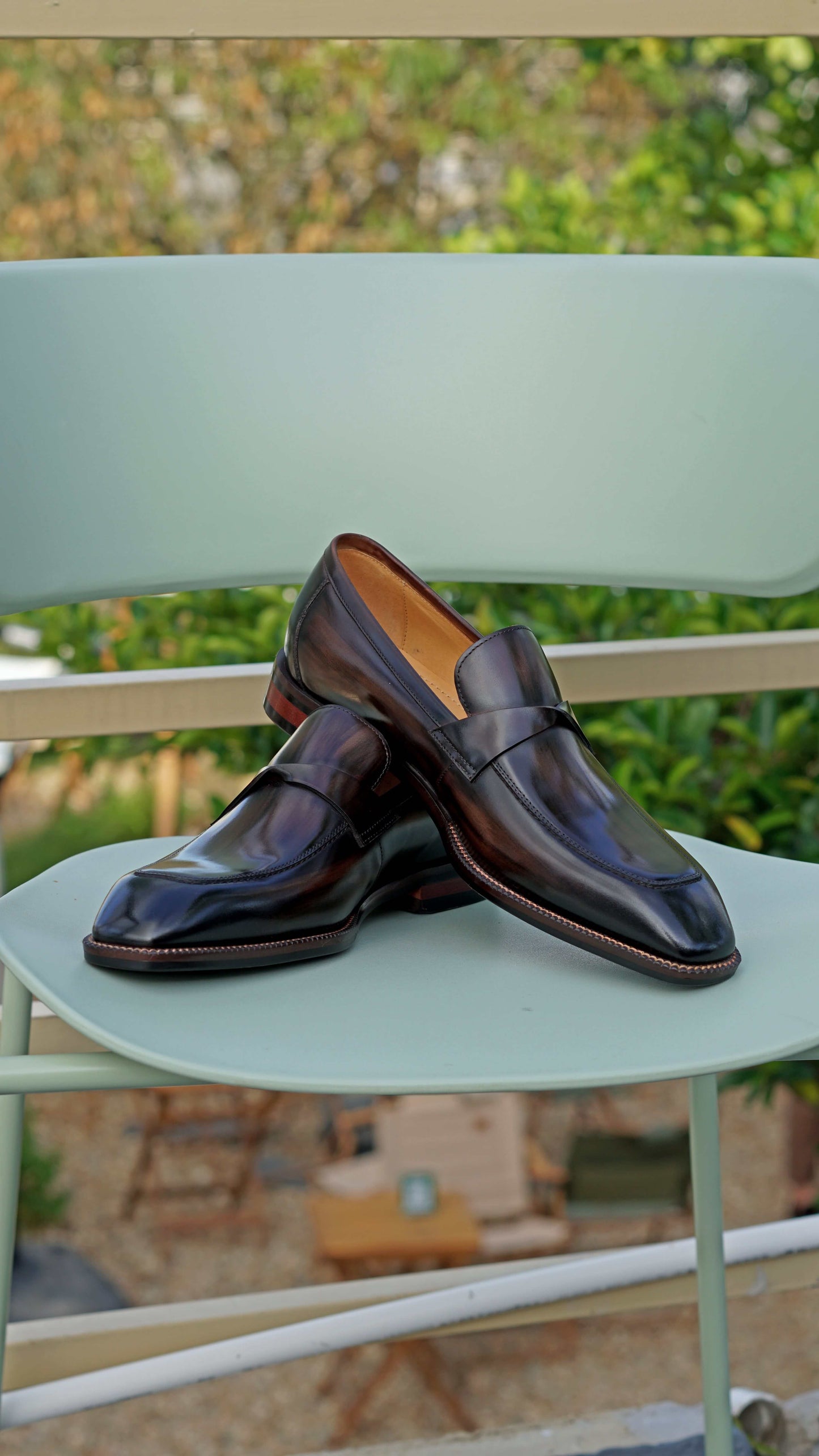 Hand-Painted Dark Brown Penny Loafers – pair on a light green chair, showcasing hand-painted patina and sleek design.