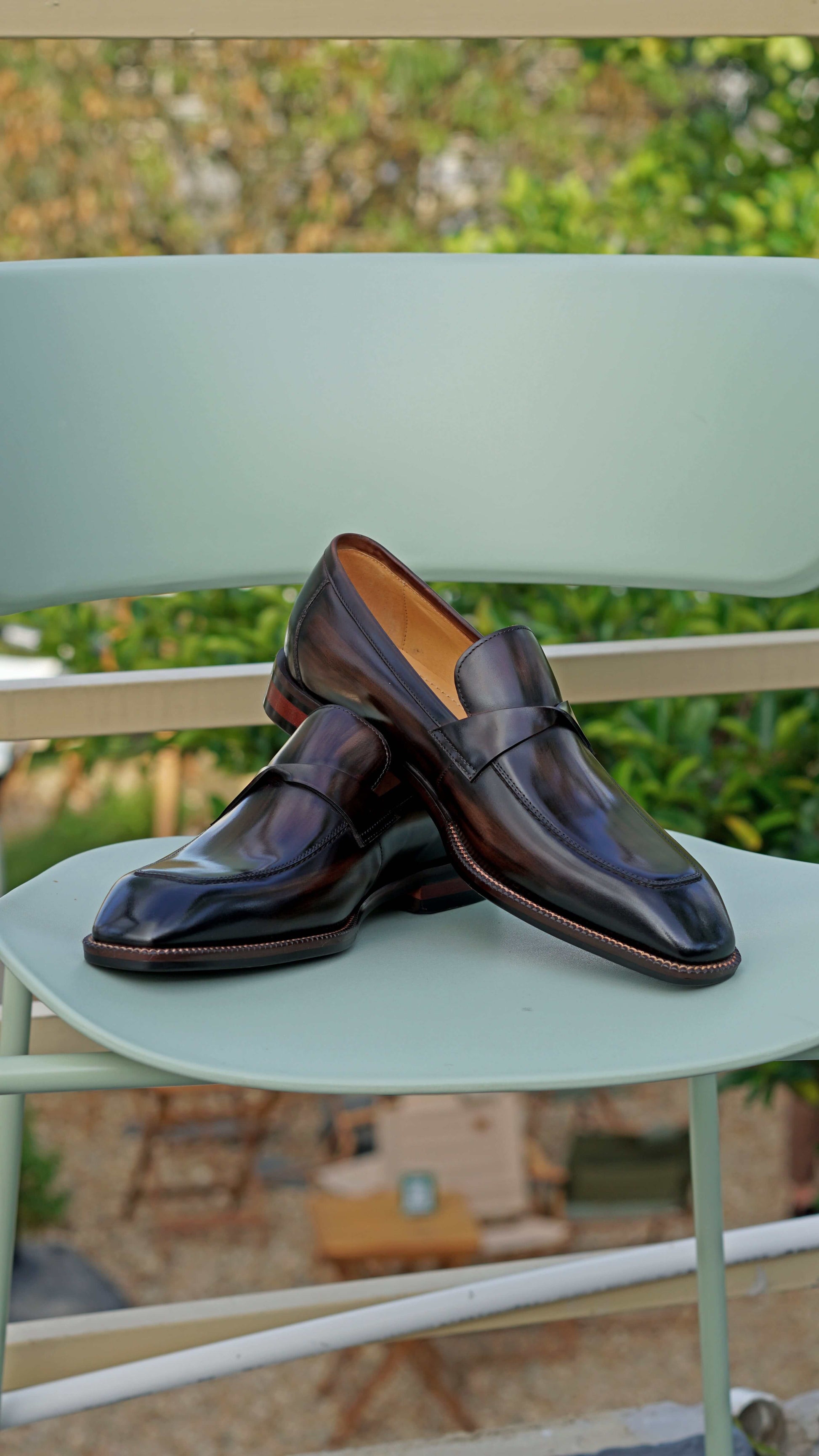 Hand-Painted Dark Brown Penny Loafers – pair on a light green chair, showcasing hand-painted patina and sleek design.