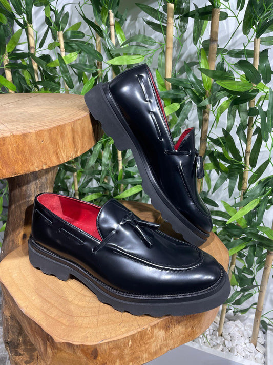  Handcrafted Black Leather Tassel Loafers with Chunky Soles – pair displayed on a wooden stand, with a red lining, emphasizing timeless style and chunky sole for a modern twist.