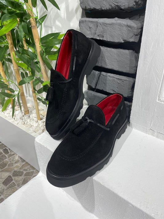 Handcrafted Black Suede Tassel Loafers with Chunky Soles – pair on a white ledge with a red lining, displaying luxurious suede and a contemporary edge.
