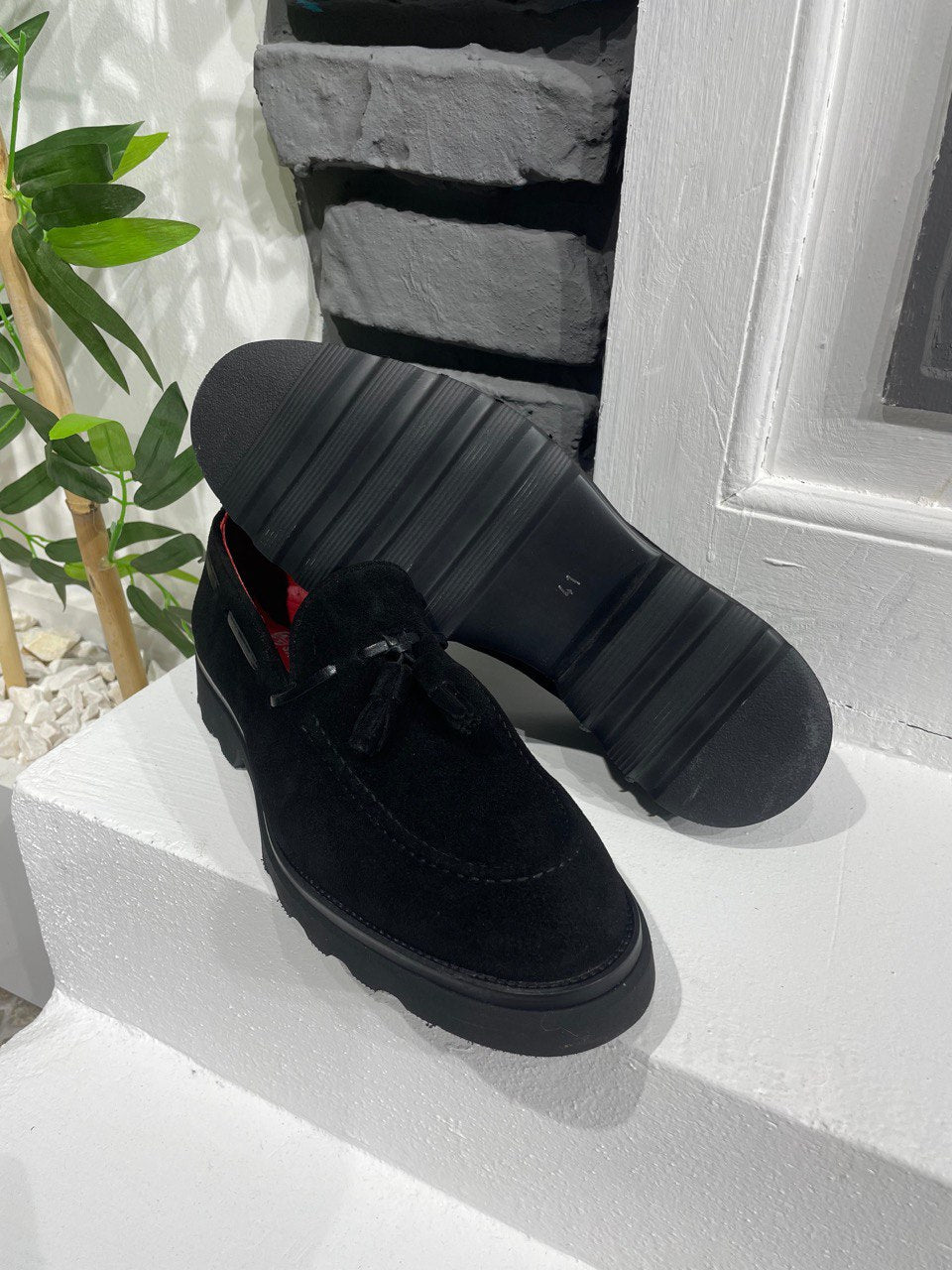 Handcrafted Black Suede Tassel Loafers with Chunky Soles – one shoe upright and one showing the sole, with red lining, showcasing premium suede and modern style.