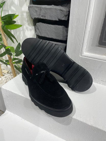 Handcrafted Black Suede Tassel Loafers with Chunky Soles – one shoe upright and one showing the sole, with red lining, showcasing premium suede and modern style.