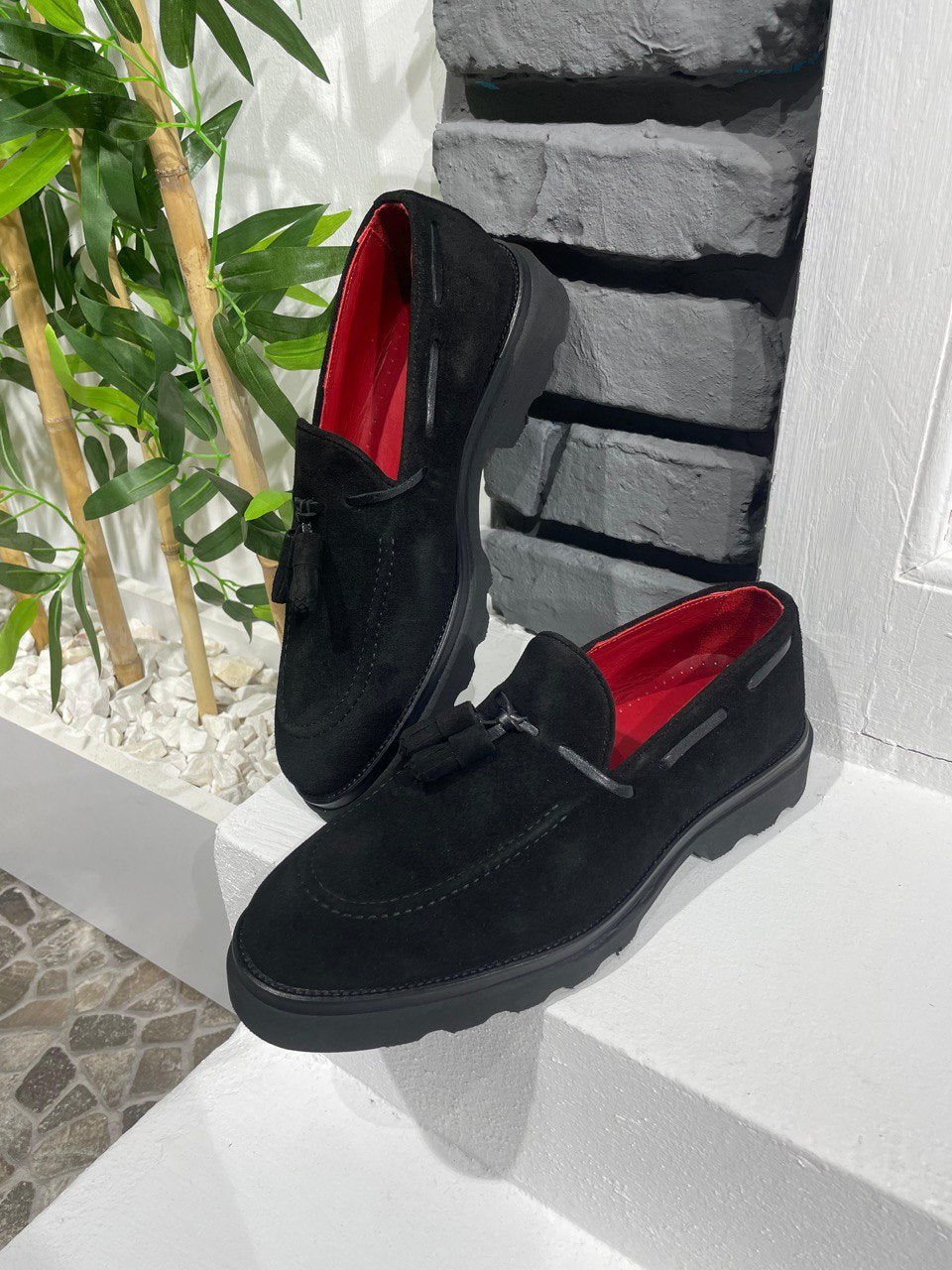 Handcrafted Black Suede Tassel Loafers with Chunky Soles – one shoe upright and one showing the sole, with red lining, showcasing chunky sole and a modern edge.