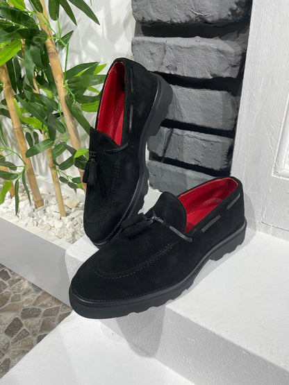 Handcrafted Black Suede Tassel Loafers with Chunky Soles – one shoe upright and one showing the sole, with red lining, showcasing chunky sole and a modern edge.