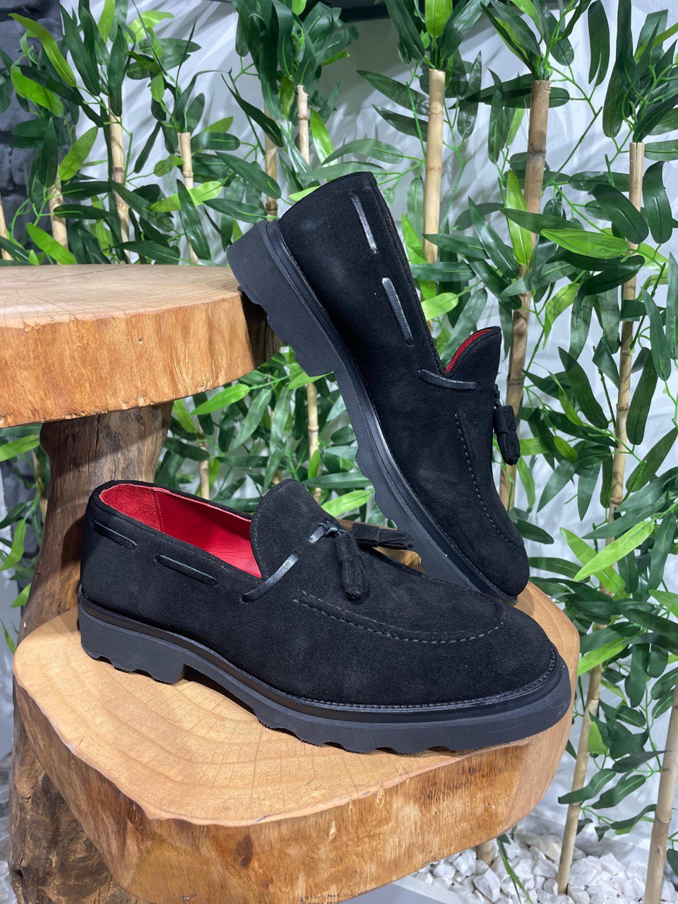 Handcrafted Black Suede Tassel Loafers with Chunky Soles – pair displayed on a wooden stump, with a red lining, emphasizing luxurious suede and contemporary style.