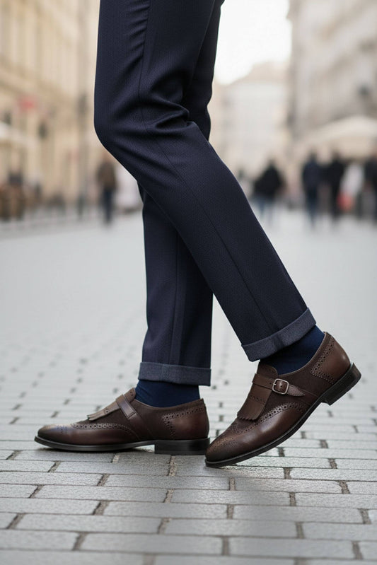 Person wearing navy pants and brown shoes on a city street.