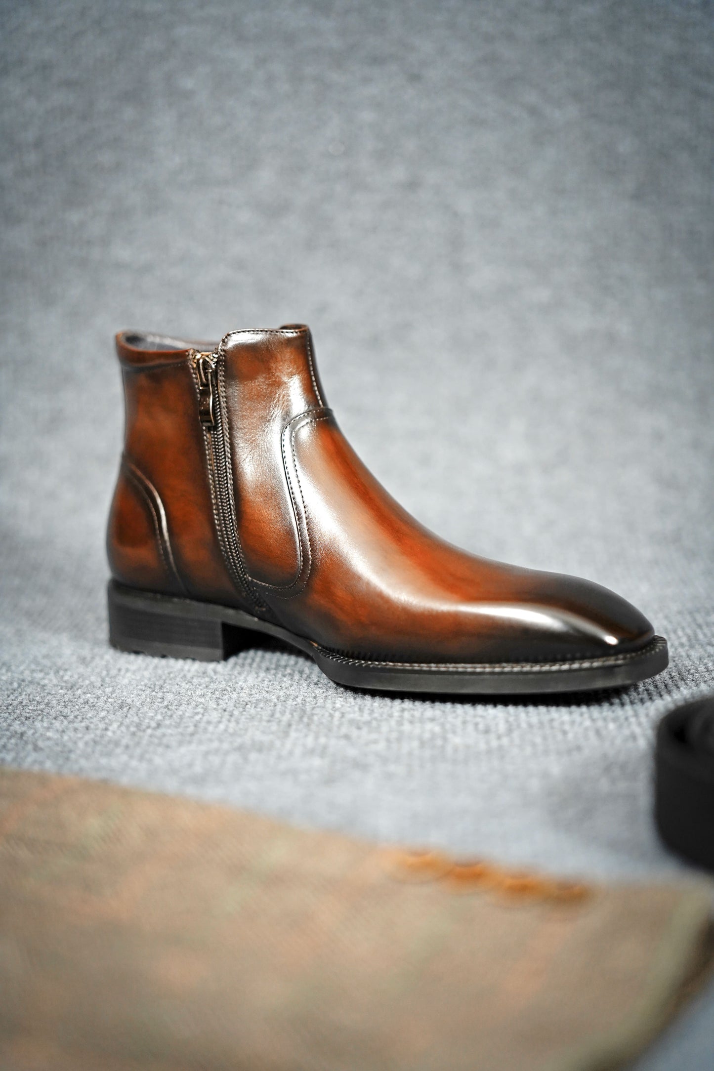 Handcrafted Brown Leather Zip-Up Ankle Boots with Buckle Detail – a full side view of a single boot on a gray textured background, showcasing the zip and buckle.