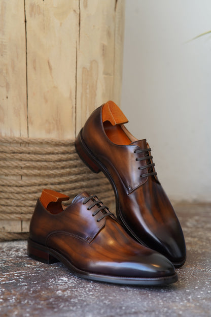 A pair of exquisite brown patina derby shoes with shoe trees, showcasing their hand-finished leather and sleek design.
