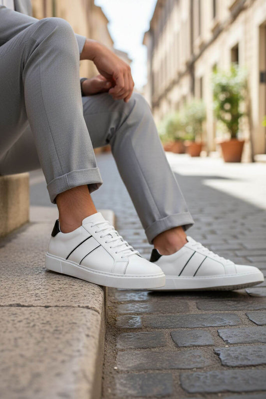 Person wearing white sneakers and gray pants sitting on a stone bench in an urban setting.
