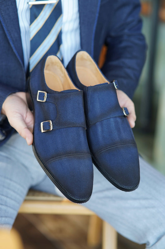 Handcrafted Navy Suede Double Monk Strap Dress Shoes – held by a man in a pinstripe suit, highlighting luxurious suede and modern elegance.