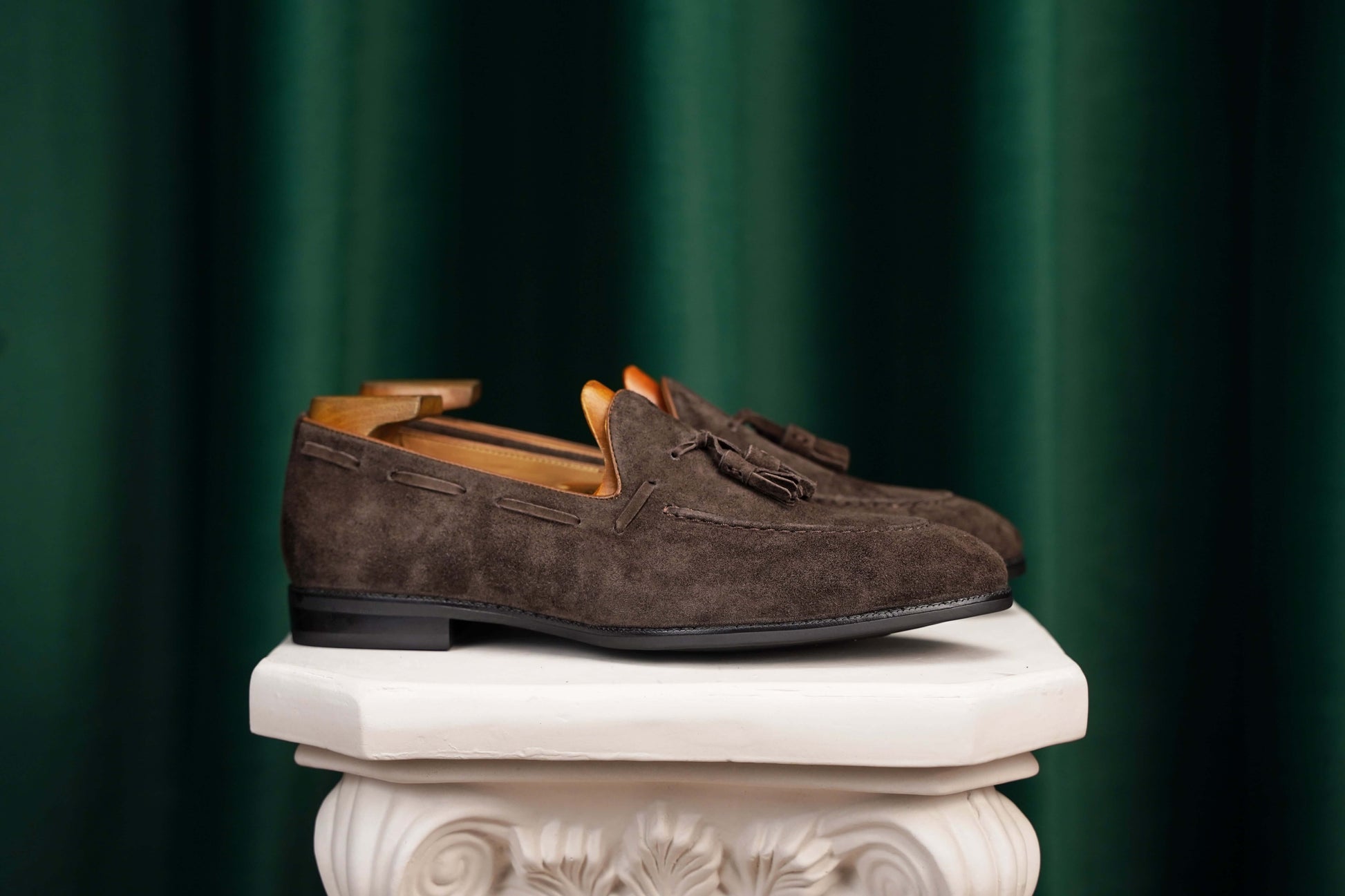 Handcrafted Umber Dark Brown Tassel Suede Loafers – pair with shoe trees, displayed on a stand, showcasing refined minimalism and soft brown suede.