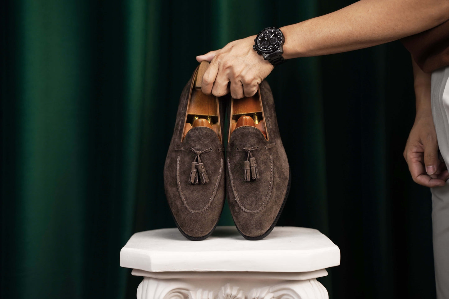 Handcrafted Umber Dark Brown Tassel Suede Loafers – pair held by a man's hand with a watch, showcasing rich dark brown suede and classic design for understated character.