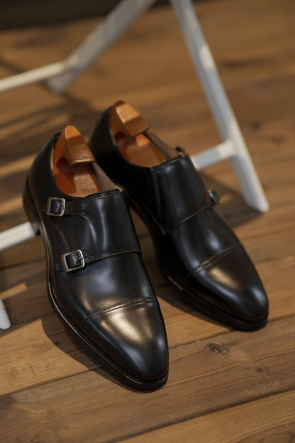 Handmade Black Double Monk Strap Dress Shoes – pair with shoe trees on a wooden floor, highlighting premium leather and polished double buckle closure.