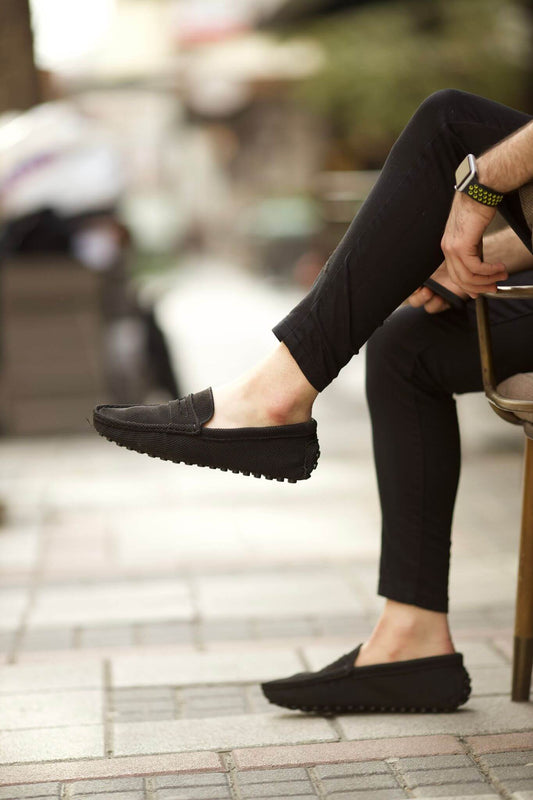 Handmade Black Knitted Driving Loafers – worn by a man in black trousers, sitting on a chair, highlighting knitted exterior and sleek silhouette.