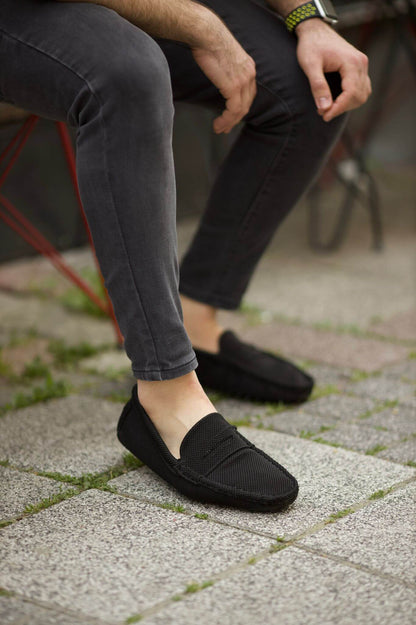 Handmade Black Knitted Driving Loafers – worn by a man in grey jeans, sitting on the ground, showcasing rubber driving sole and comfortable fit.