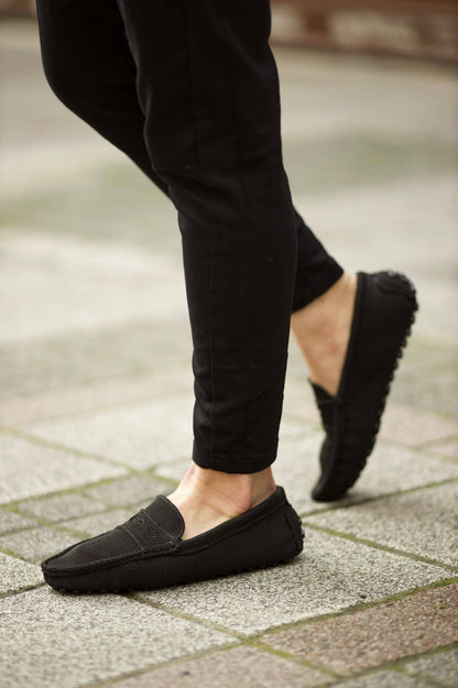 Handmade Black Knitted Driving Loafers – worn by a man in black trousers, walking on a paved ground, highlighting knitted texture and rubber driving sole.