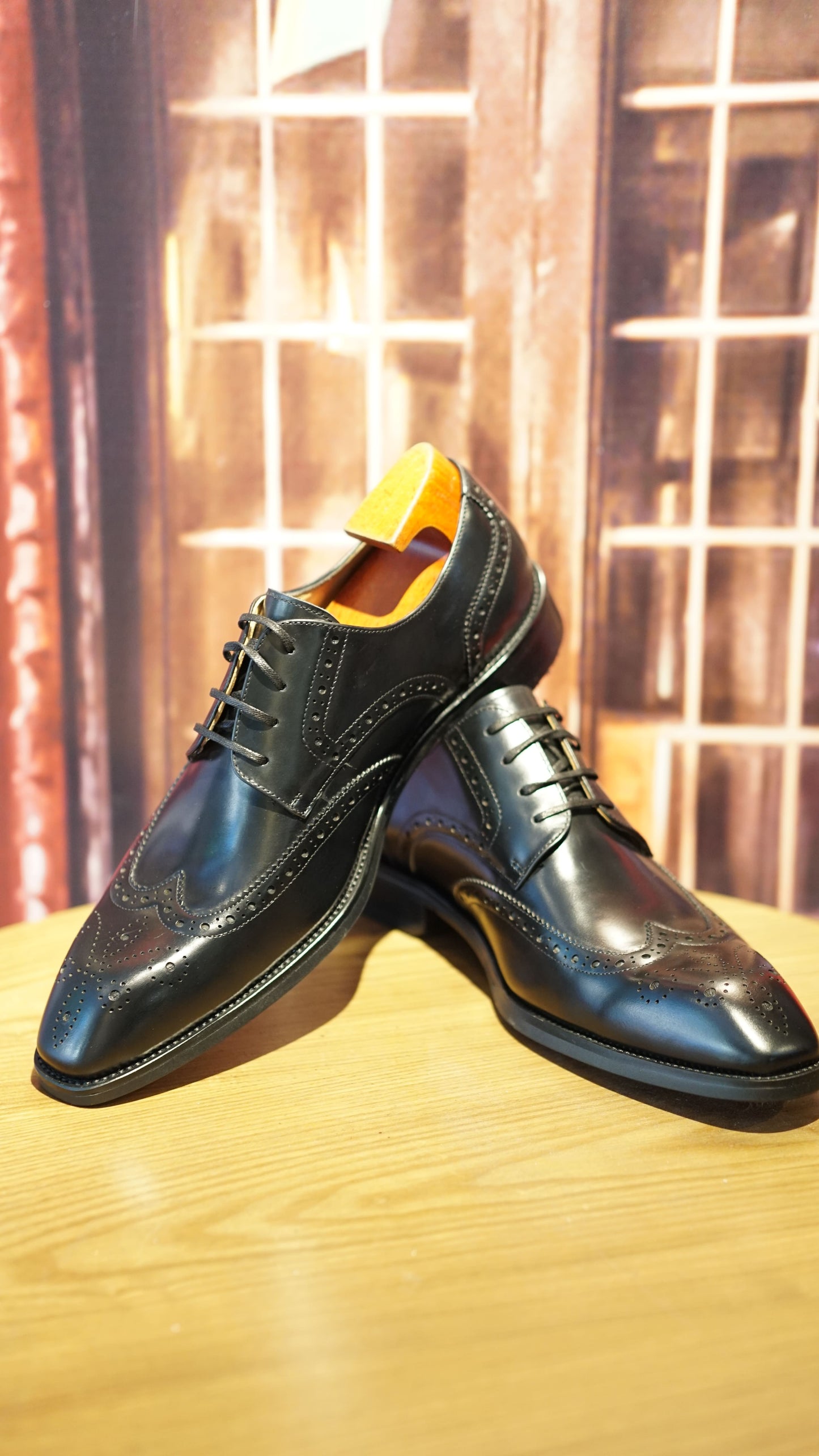 Handmade Black Wingtip Derby Shoes – premium polished leather, pair displayed on a wooden surface with intricate brogue detailing and shoe trees.