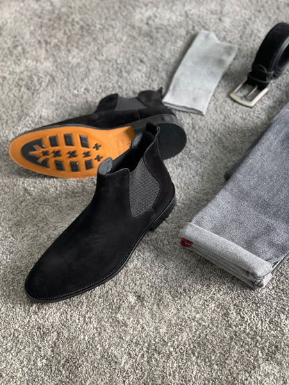 Handmade Classic Black Suede Chelsea Boots – a pair of boots with a belt and socks, with one boot turned on its side to display the sole.