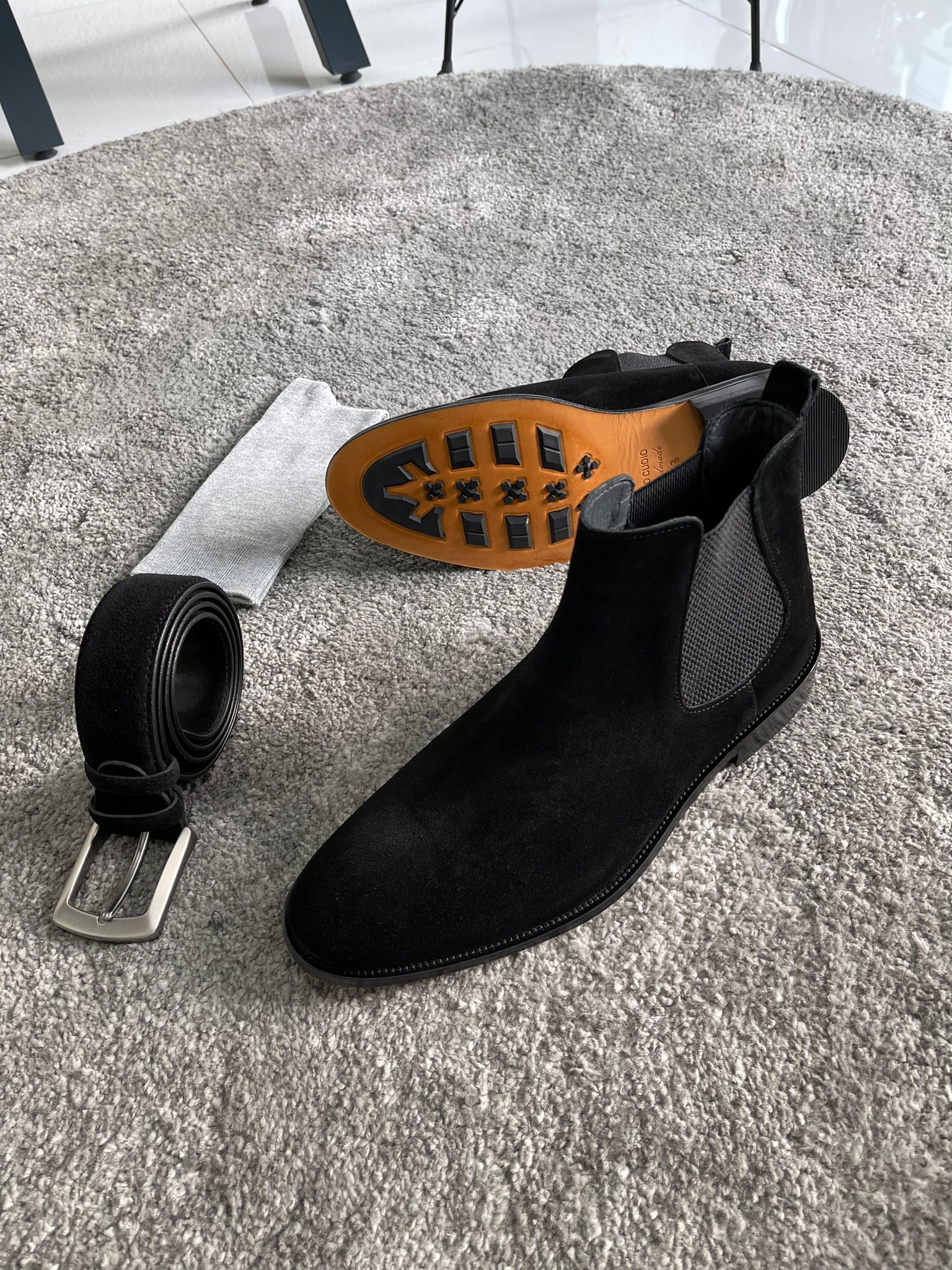 Handmade Classic Black Suede Chelsea Boots – a pair of black suede Chelsea boots and gray pants, with one boot turned to show the orange-colored sole.