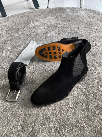 Handmade Classic Black Suede Chelsea Boots – a pair of black suede Chelsea boots and gray pants, with one boot turned to show the orange-colored sole.