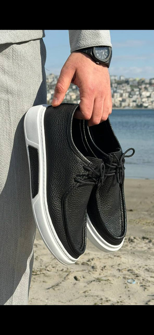 Person holding a black sneaker with white sole on a beach.