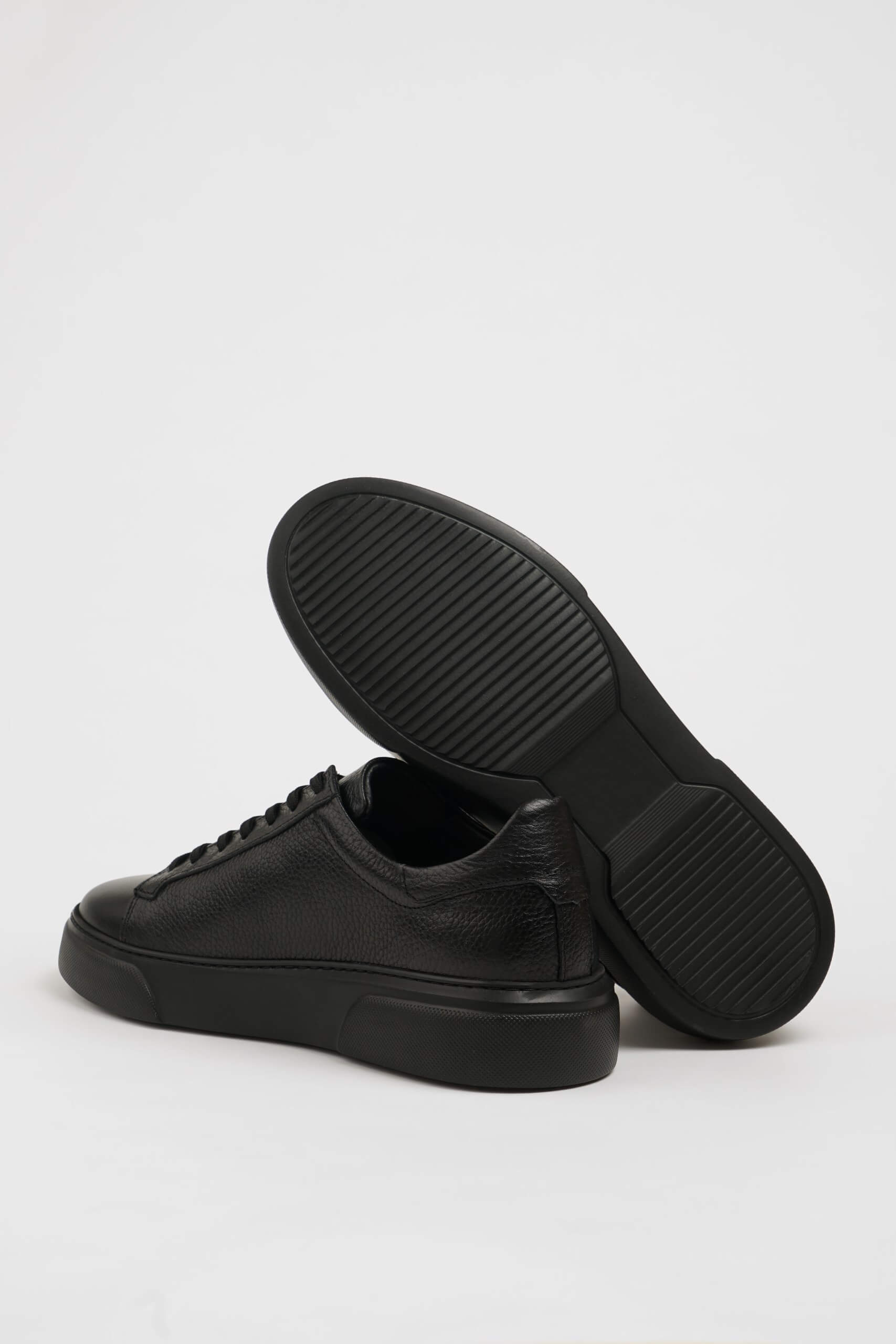 All Black Grained Leather Sneakers for Minimalist Style – one shoe showing the textured black sole for reliable traction, the other upright.