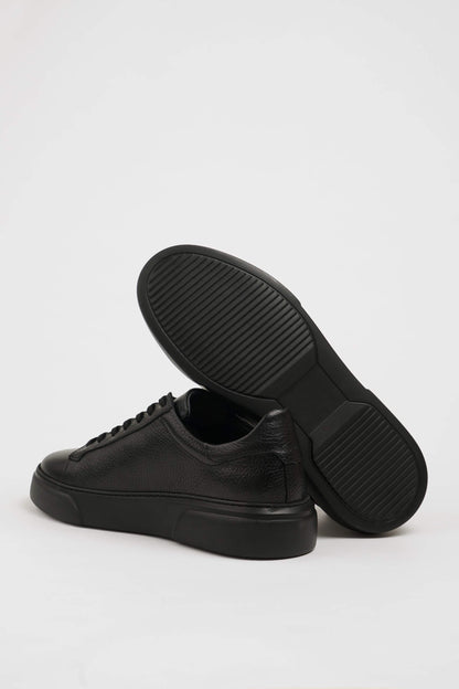 All Black Grained Leather Sneakers for Minimalist Style – one shoe showing the textured black sole for reliable traction, the other upright.