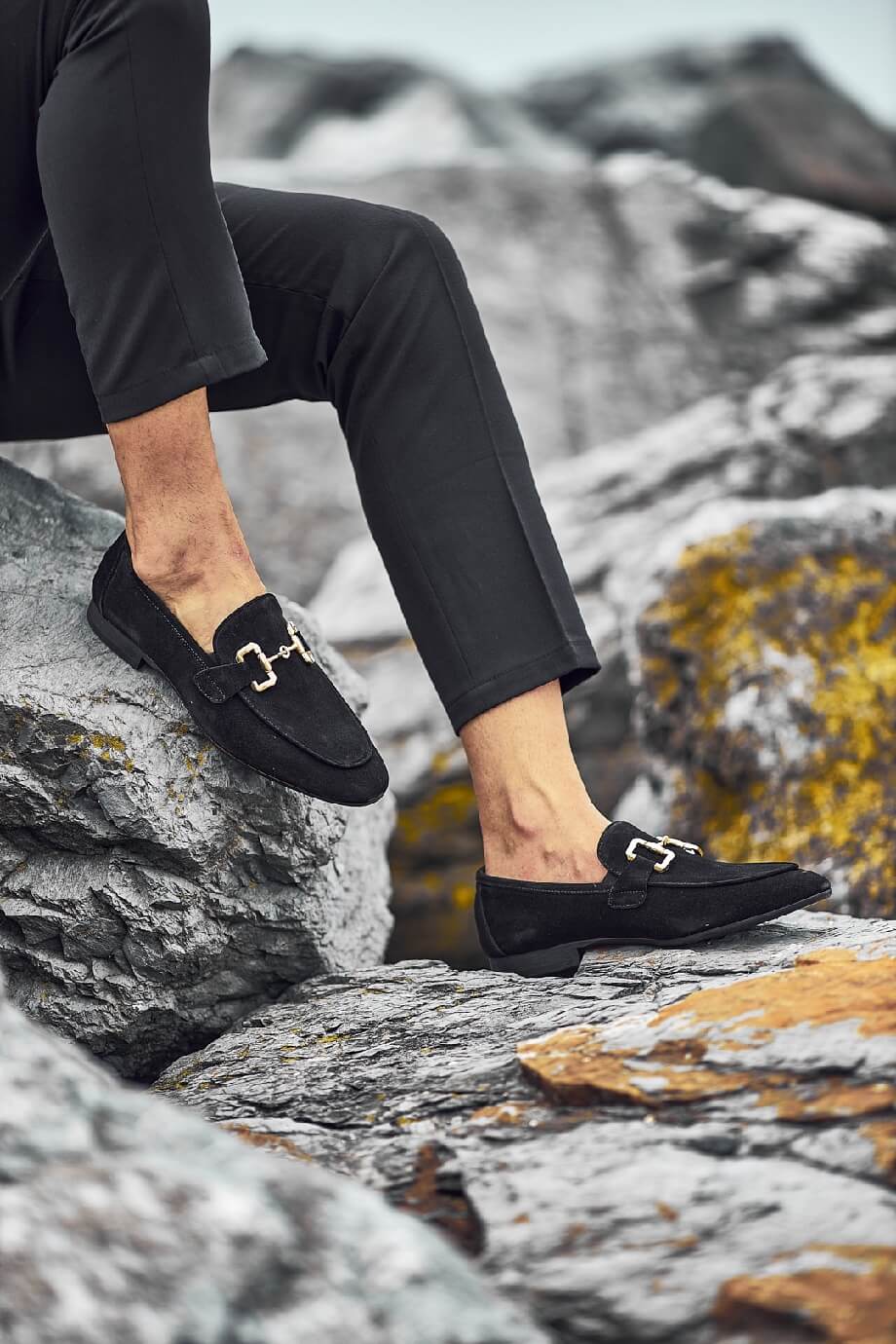 HolloShoe Black Suede Horsebit Loafers for Business & Casual Wear – classic horsebit detail, worn with black trousers, sitting on a rocky surface, showcasing versatility.