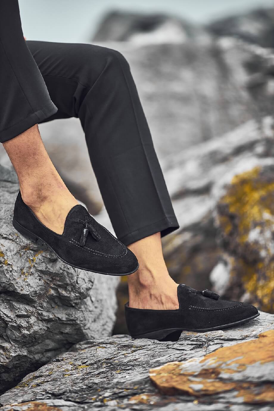 HolloShoe Black Suede Tassel Loafers - Sophisticated Leather Footwear – worn by a man in black trousers, sitting on a rock, highlighting premium suede and classic tassel detail.