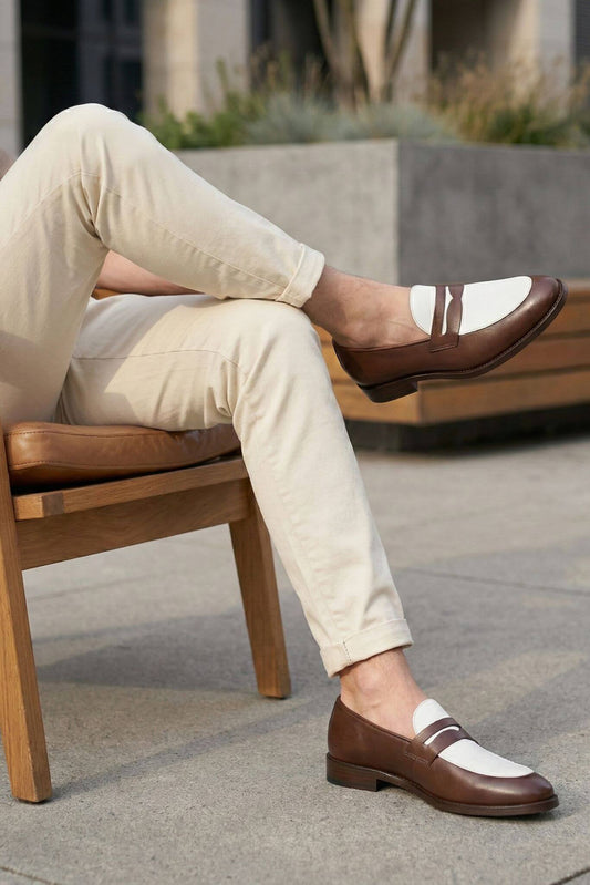 Person wearing brown and white loafers sitting on a wooden chair outdoors.