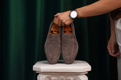 Earth Brown Suede Penny Loafers – pair held by a man's hand with a watch, highlighting soft brown suede and classic design.