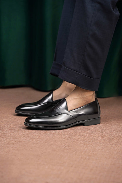 HolloShoe Handmade Black Leather Penny Loafers – worn by a man in cuffed navy trousers, standing on a patterned rug, highlighting sleek black leather for refined styling.