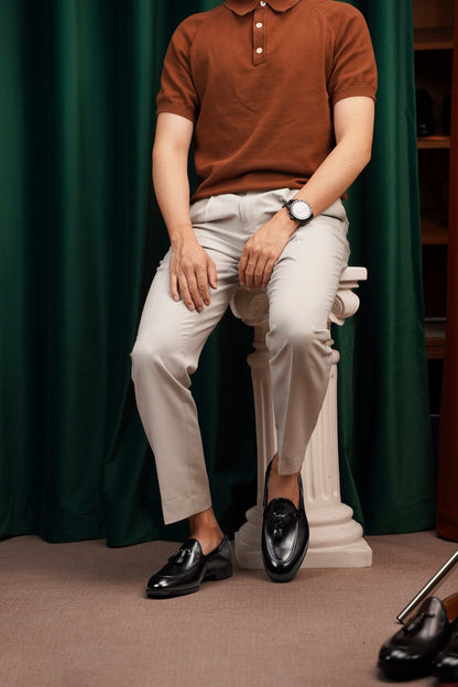 HolloShoe Handmade Black Tassel Leather Loafers – worn by a man in light trousers and polo shirt, sitting on a stone pedestal, ideal for smart casual events.