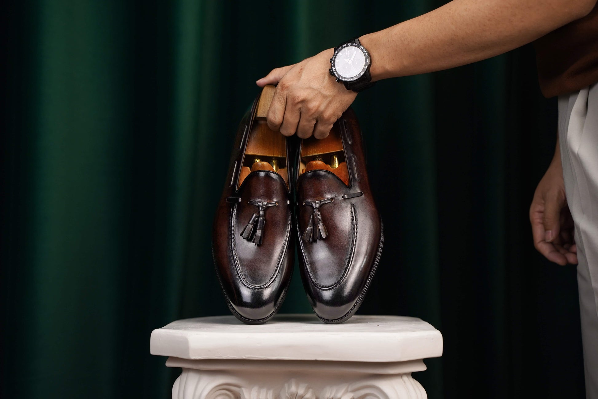 HolloShoe Handmade Chestnut Brown Patina Tassel Loafers – pair held by a man's hand with a watch, showcasing rich brown patina and signature tassels