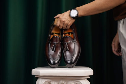 HolloShoe Handmade Chestnut Brown Patina Tassel Loafers – pair held by a man's hand with a watch, showcasing rich brown patina and signature tassels