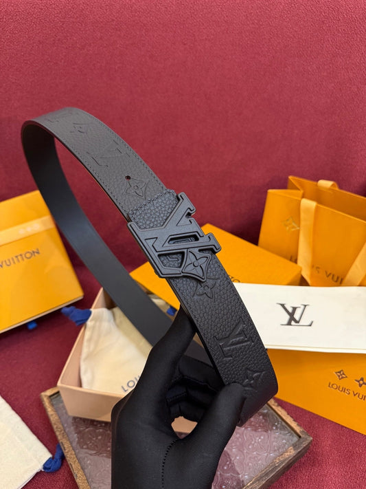 Black belt with a prominent buckle held by a gloved hand against a maroon background with Louis Vuitton packaging.