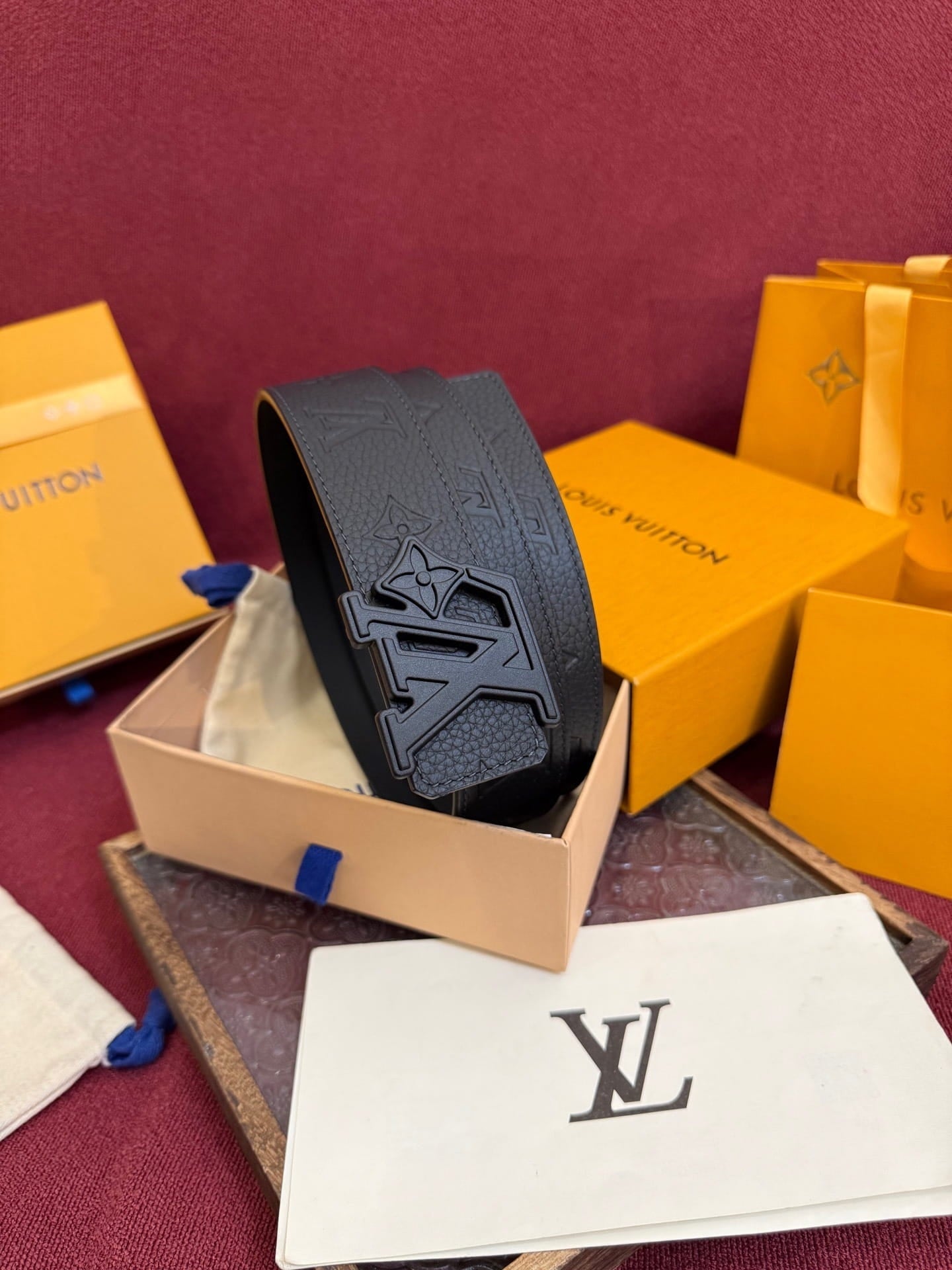 Black belt with logo on a red surface with Louis Vuitton packaging.