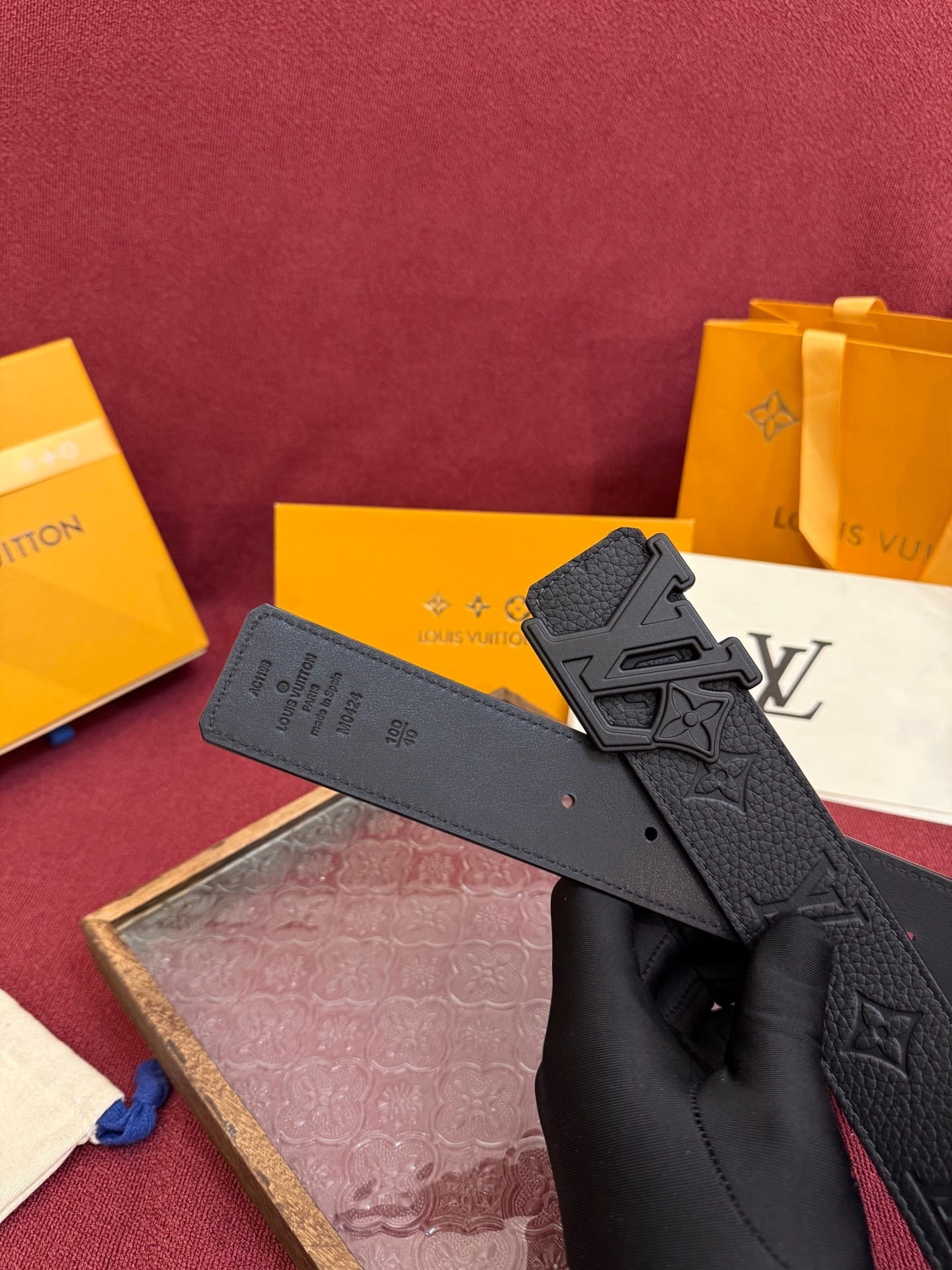 Black belt with brand logo held by a gloved hand against a red background with branded boxes.