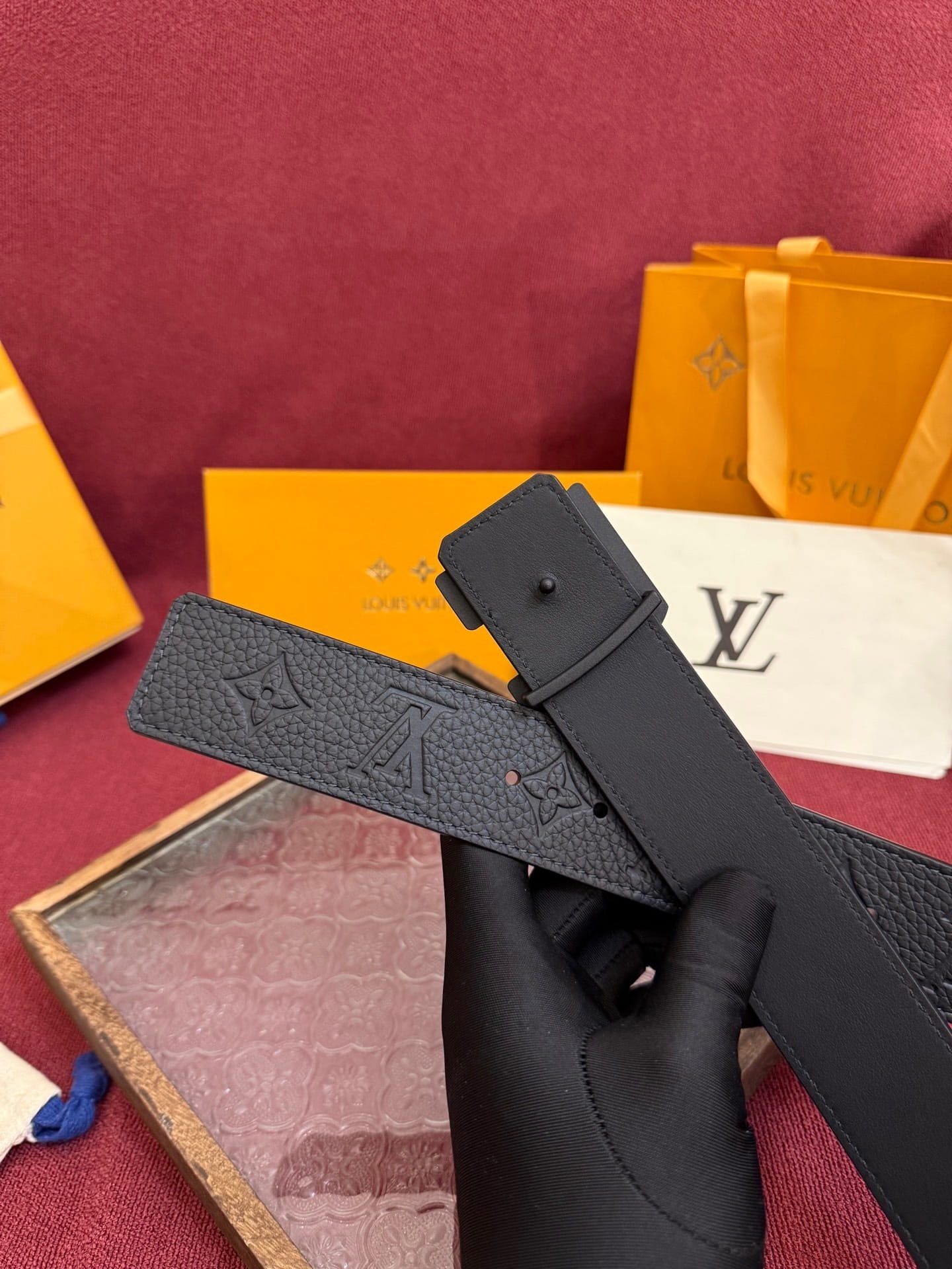 Black belt with brand logo held by a gloved hand against a maroon background with branded boxes.