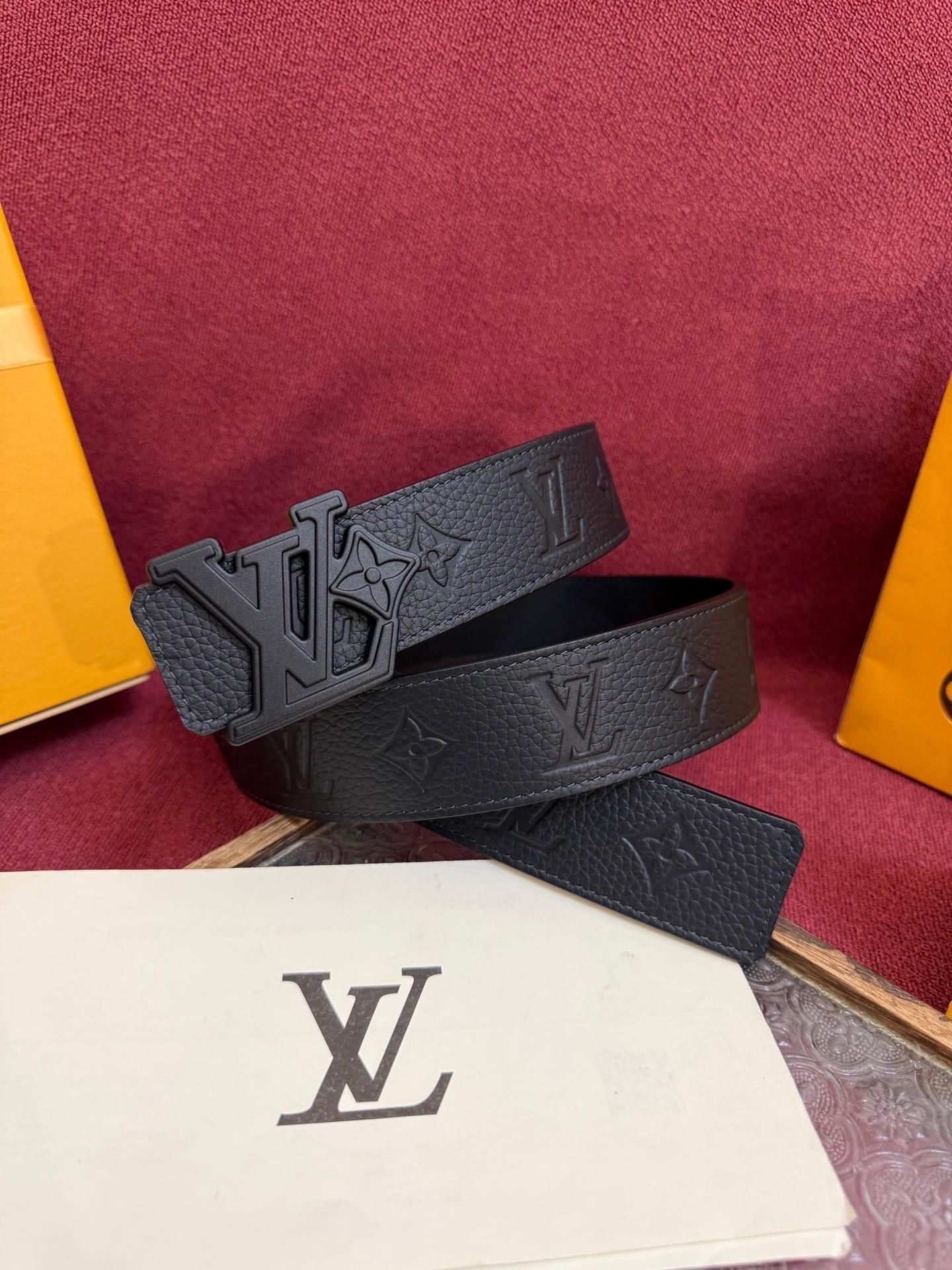 Black leather belt with brand logo on a red surface