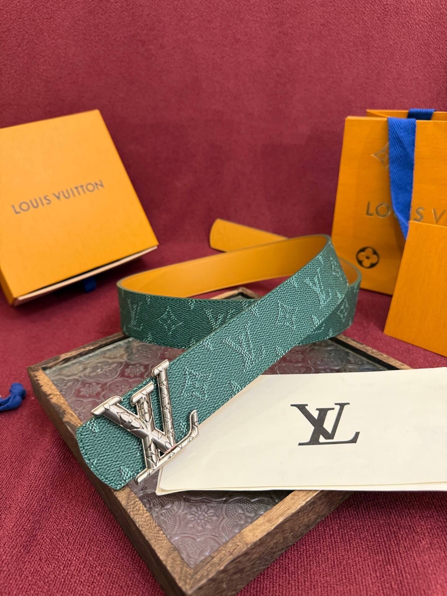 Louis Vuitton belt with monogram pattern on a red surface with branded boxes.