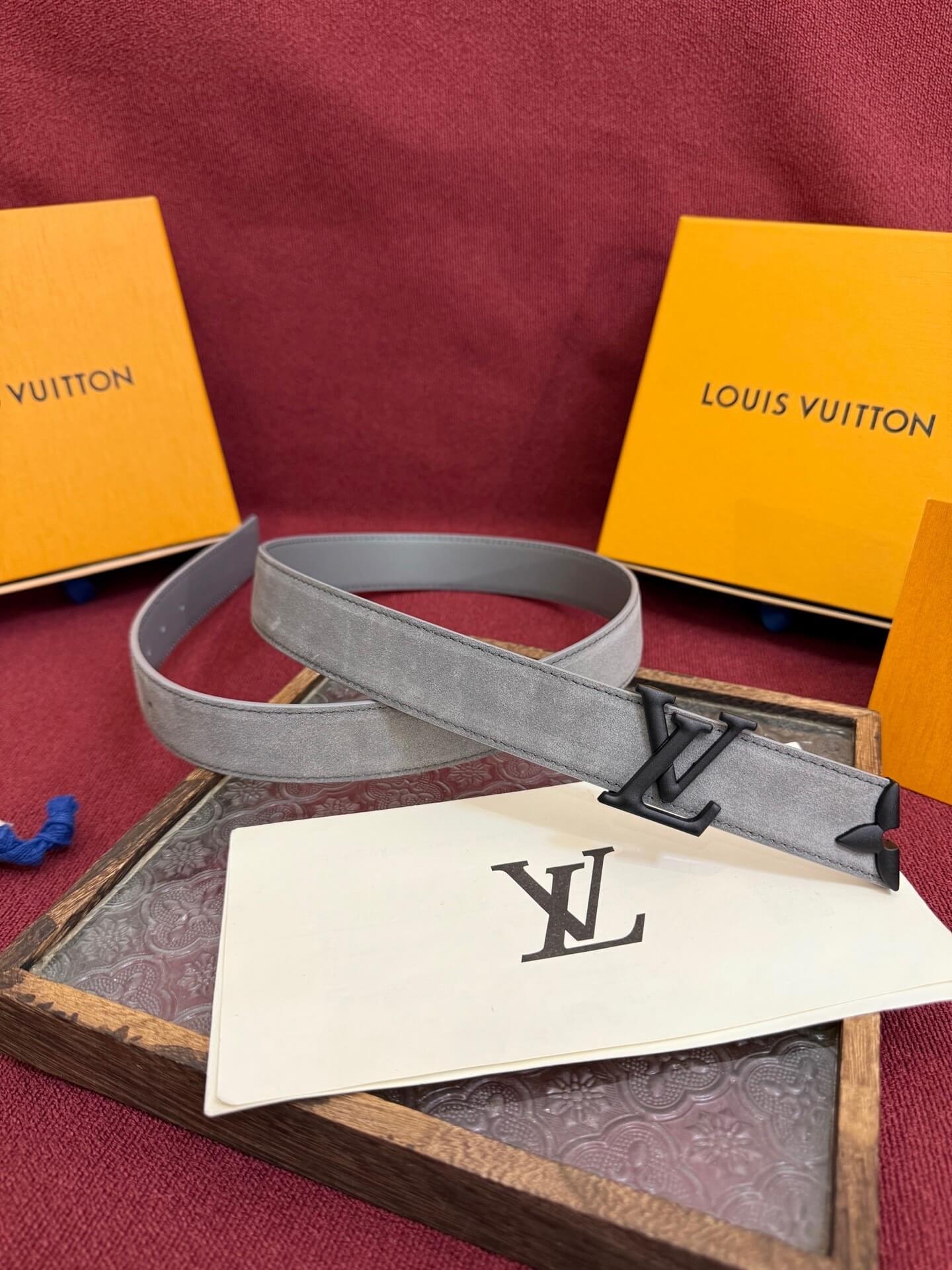 Louis Vuitton belt with monogram pattern on a red surface with branded boxes.