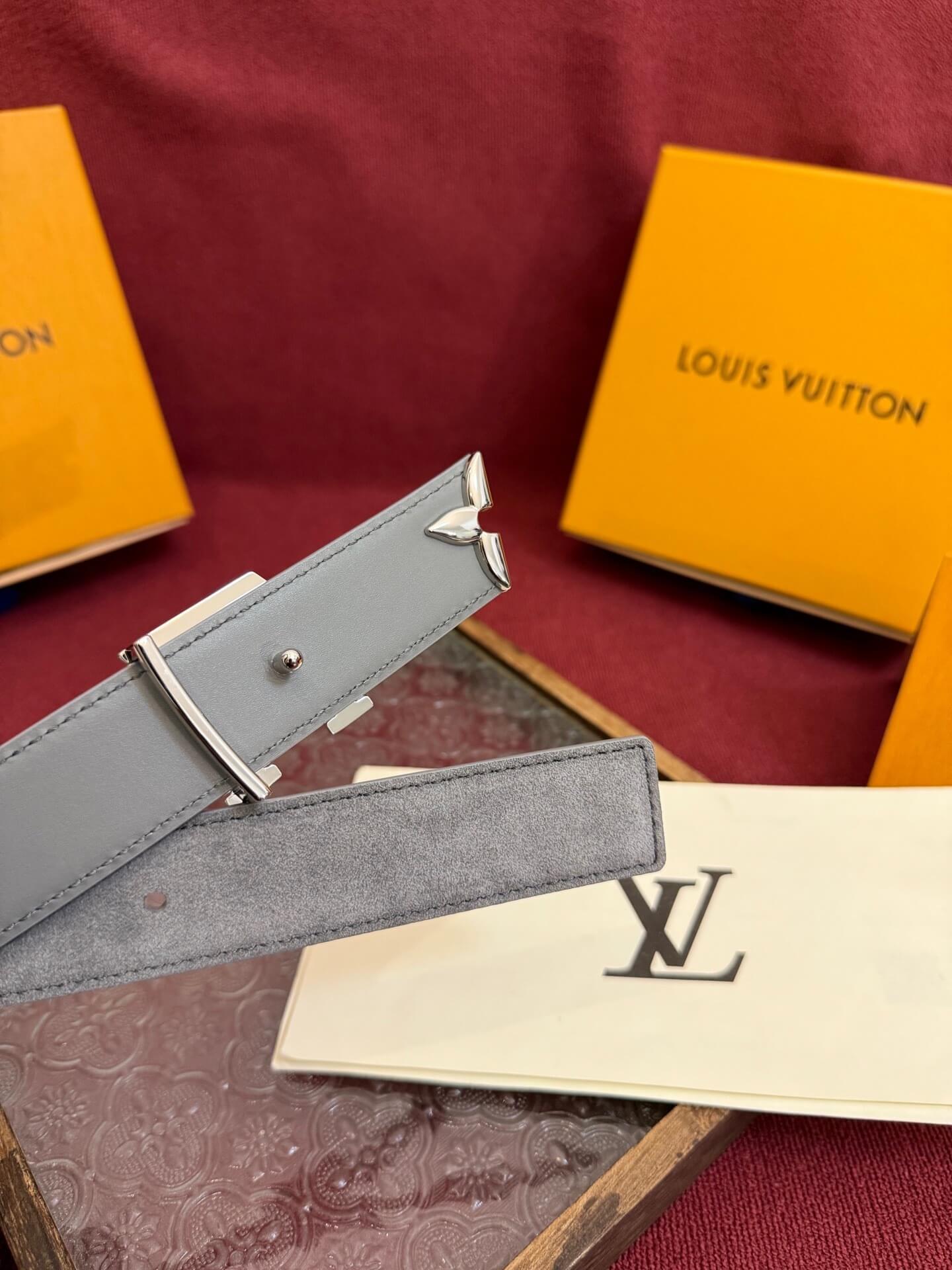 Gray belt with silver buckle on a red surface with Louis Vuitton packaging.