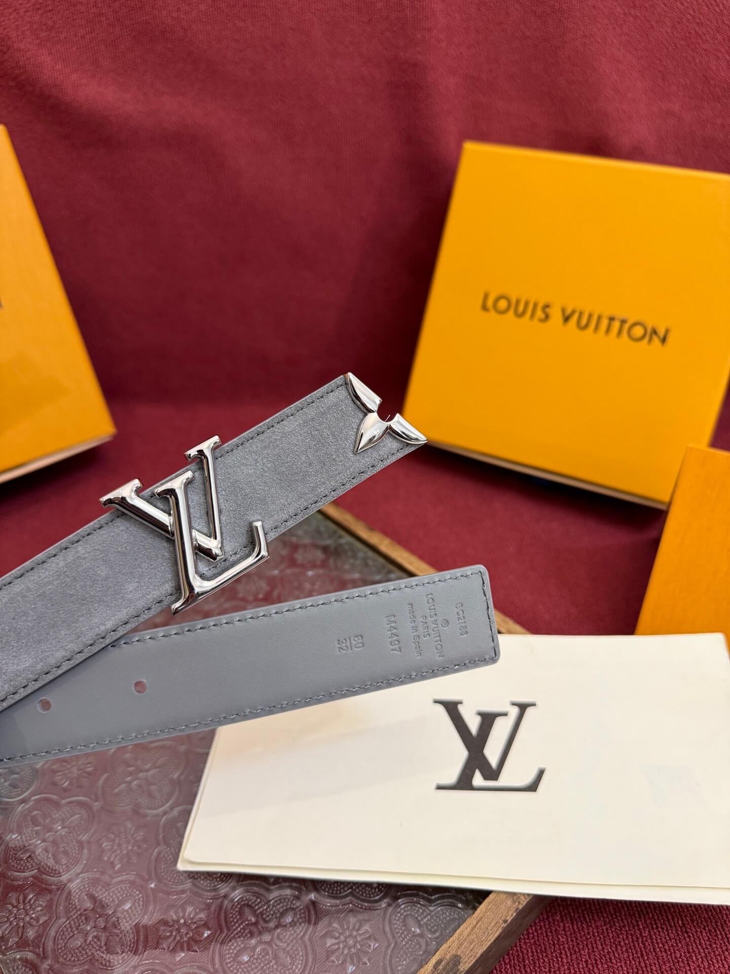 Louis Vuitton belt with silver buckle on a red surface with brand packaging.